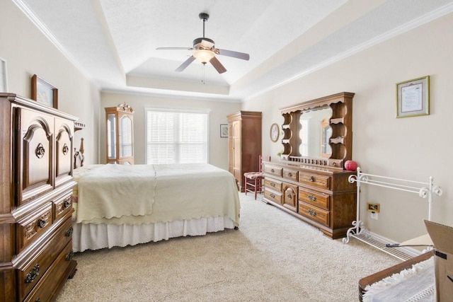 bedroom featuring ceiling fan, ornamental molding, a tray ceiling, and light carpet