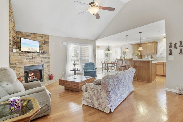 living room with vaulted ceiling, a stone fireplace, ceiling fan, and light hardwood / wood-style floors