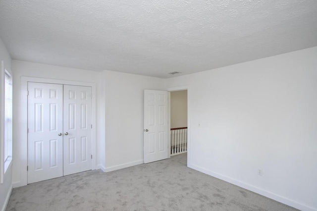 unfurnished bedroom with light carpet, a textured ceiling, and a closet