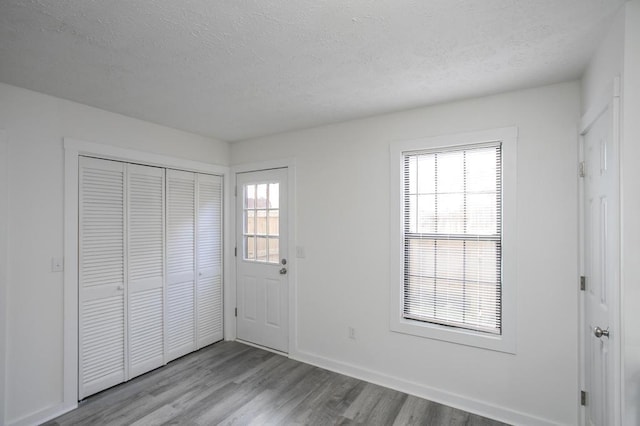 unfurnished bedroom with a closet, light hardwood / wood-style floors, multiple windows, and a textured ceiling