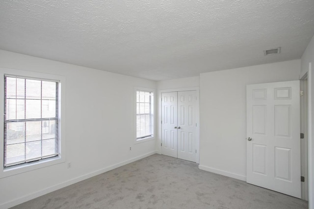 unfurnished bedroom with a closet, light carpet, and a textured ceiling