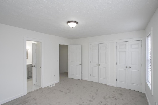 unfurnished bedroom with multiple closets, ensuite bathroom, light carpet, and a textured ceiling