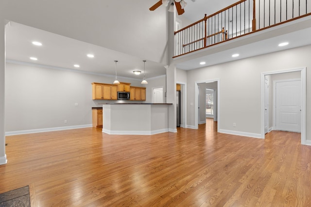 unfurnished living room with crown molding, a towering ceiling, light hardwood / wood-style flooring, and ceiling fan