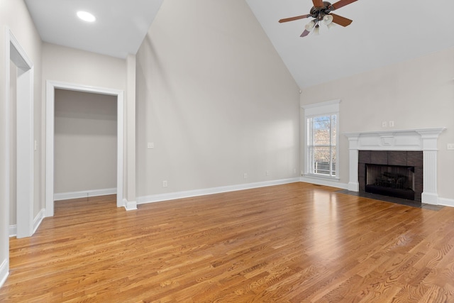 unfurnished living room with ceiling fan, a fireplace, high vaulted ceiling, and light hardwood / wood-style flooring