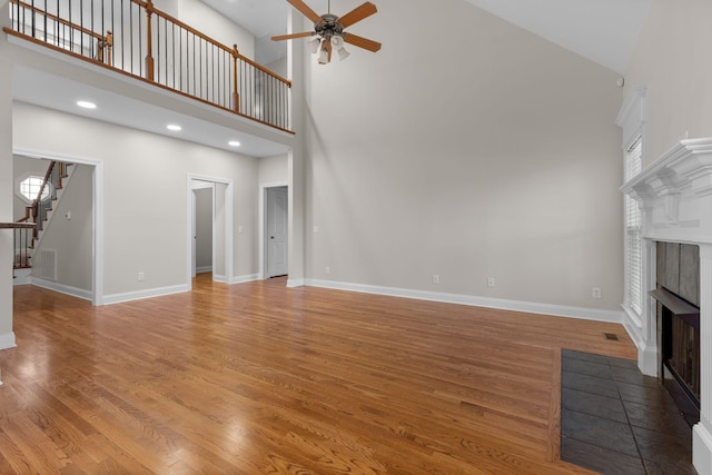 unfurnished living room with ceiling fan, a towering ceiling, wood-type flooring, and a fireplace