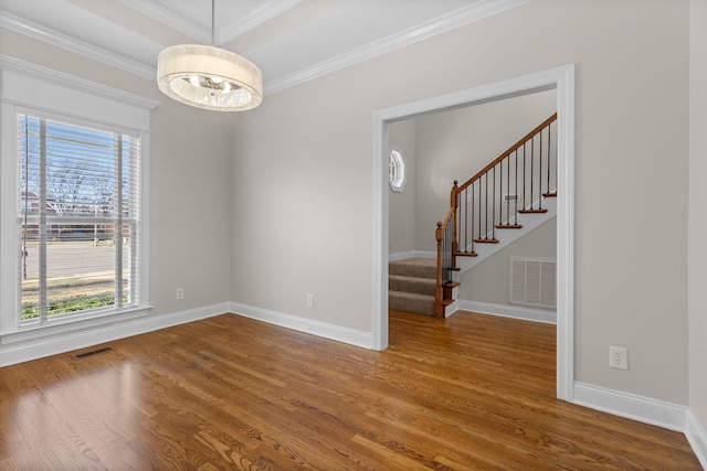 empty room with hardwood / wood-style flooring, ornamental molding, a raised ceiling, and an inviting chandelier