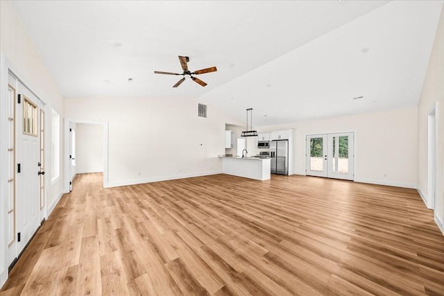 unfurnished living room featuring lofted ceiling, french doors, ceiling fan, and light wood-type flooring