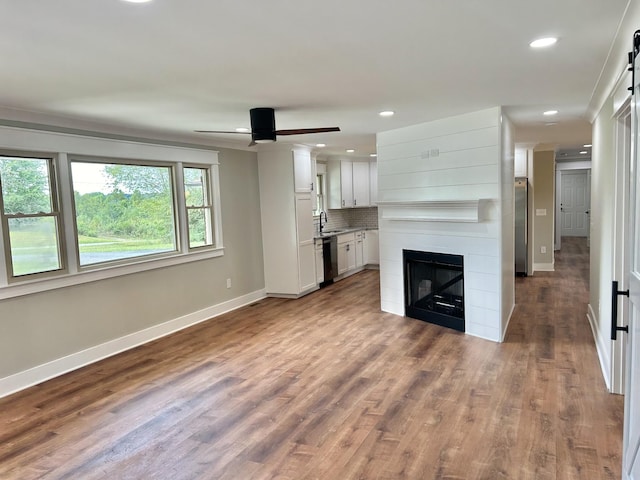 unfurnished living room with sink, hardwood / wood-style flooring, ceiling fan, a large fireplace, and a barn door