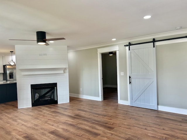 unfurnished living room with ceiling fan, a fireplace, wood-type flooring, and a barn door