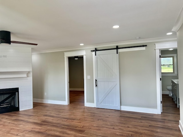 unfurnished living room with crown molding, ceiling fan, a fireplace, wood-type flooring, and a barn door