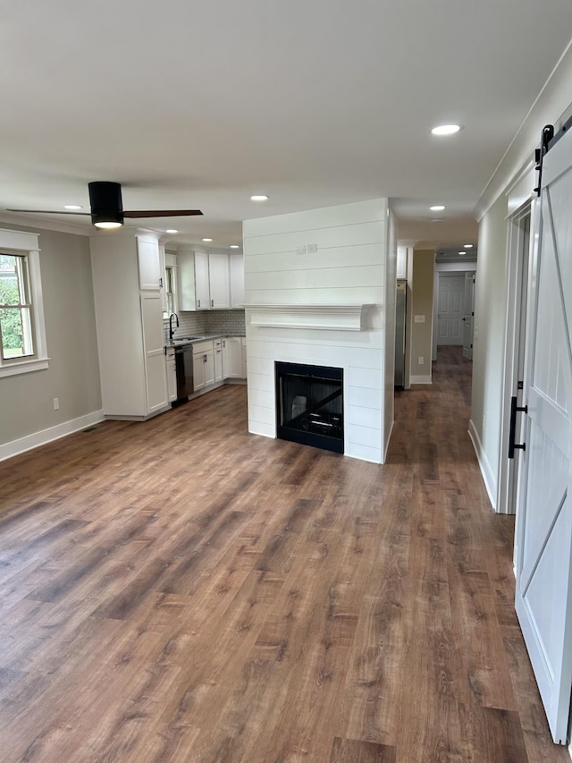 unfurnished living room with sink, dark wood-type flooring, ceiling fan, a fireplace, and a barn door