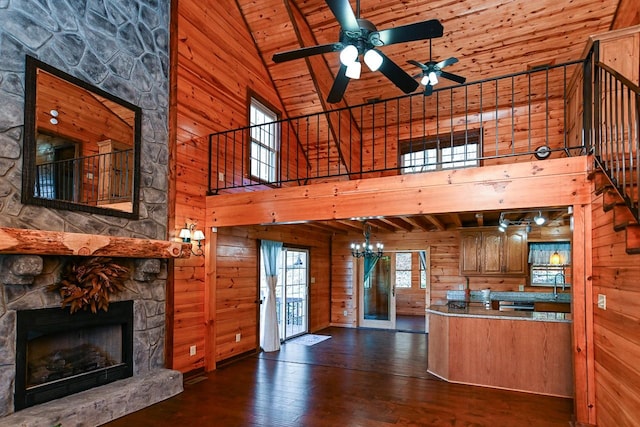 kitchen with a stone fireplace, plenty of natural light, high vaulted ceiling, and wooden walls