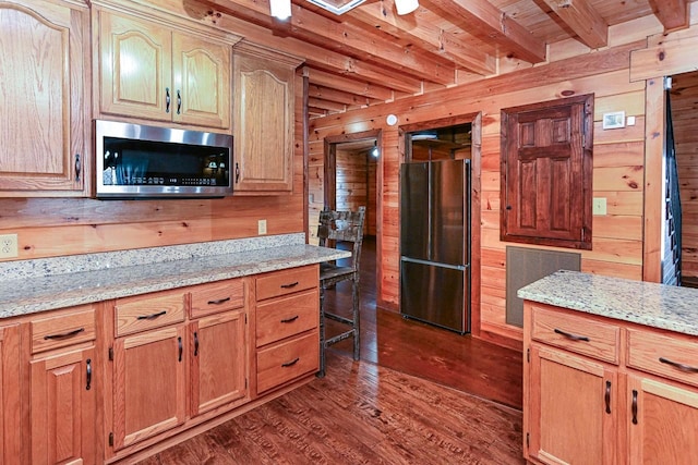 kitchen featuring light stone countertops, wood walls, beamed ceiling, and appliances with stainless steel finishes