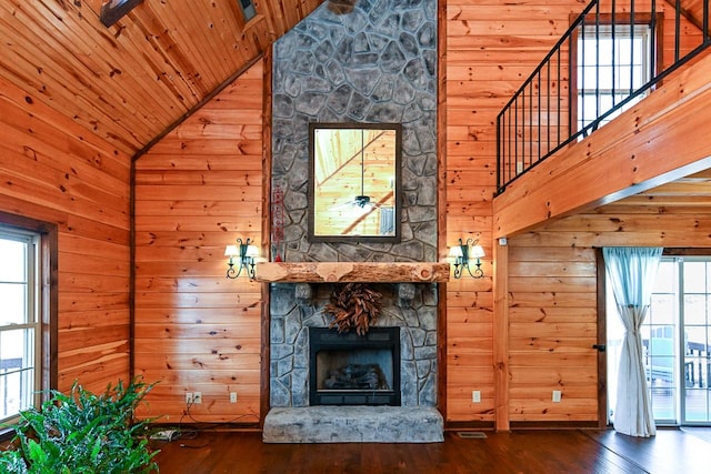 unfurnished living room featuring a stone fireplace, wooden walls, and high vaulted ceiling