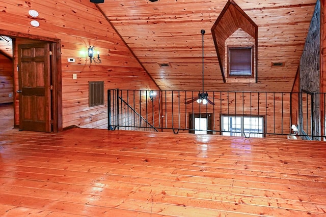 unfurnished living room with wood walls, lofted ceiling, hardwood / wood-style flooring, ceiling fan, and wood ceiling