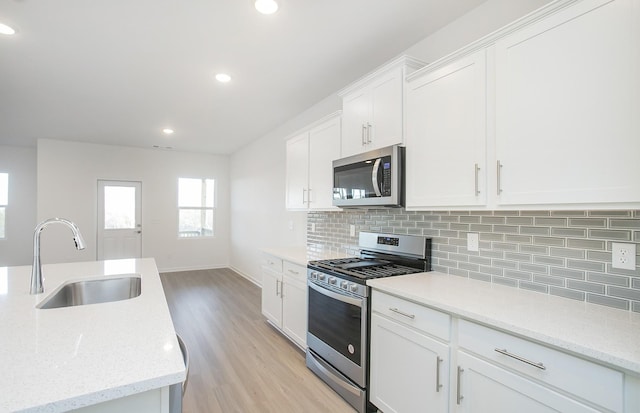 kitchen featuring sink, stainless steel appliances, light stone countertops, light hardwood / wood-style floors, and white cabinets