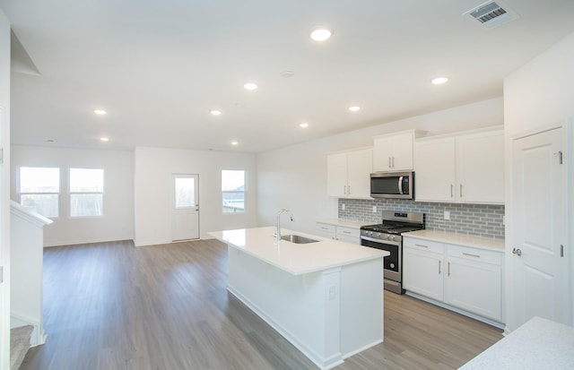 kitchen featuring appliances with stainless steel finishes, white cabinetry, sink, a center island with sink, and light hardwood / wood-style flooring