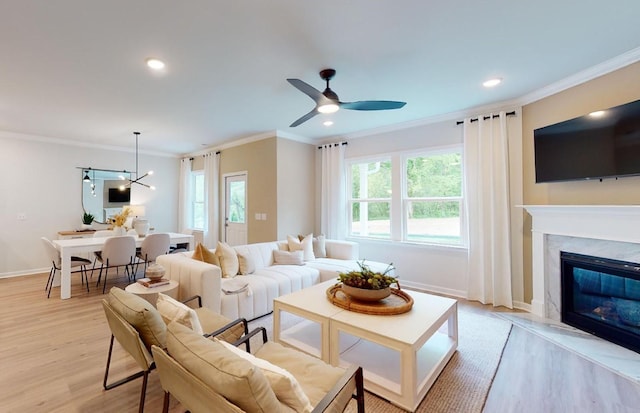 living room featuring a high end fireplace, light hardwood / wood-style flooring, ornamental molding, and ceiling fan with notable chandelier