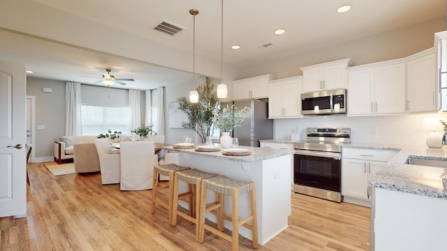 kitchen with appliances with stainless steel finishes, pendant lighting, white cabinets, and light hardwood / wood-style flooring