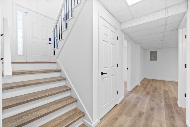 stairs featuring hardwood / wood-style floors, a drop ceiling, and electric panel