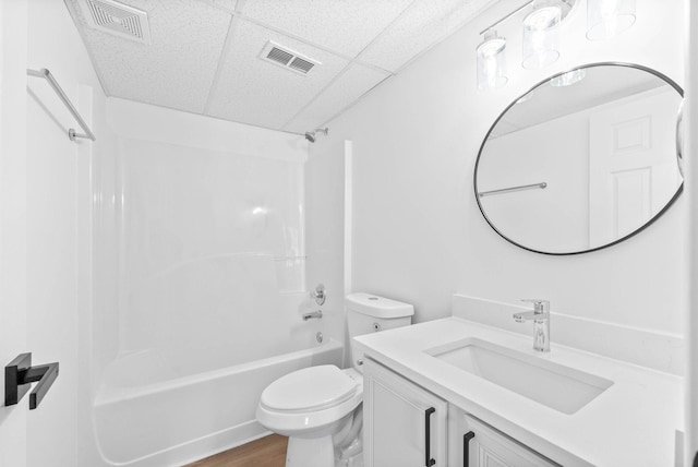 full bathroom with hardwood / wood-style flooring, vanity, a drop ceiling, shower / washtub combination, and toilet