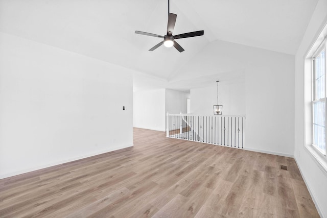 spare room with plenty of natural light, ceiling fan with notable chandelier, lofted ceiling, and light hardwood / wood-style flooring