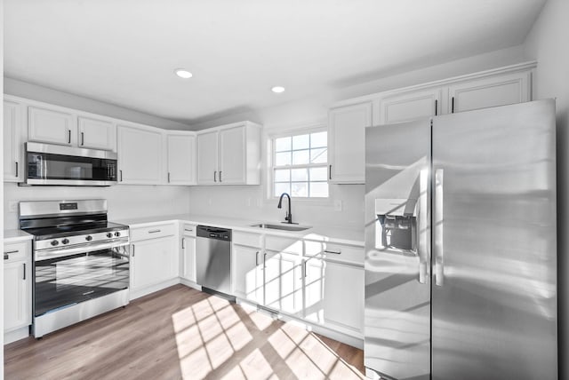 kitchen with sink, light hardwood / wood-style flooring, stainless steel appliances, and white cabinets