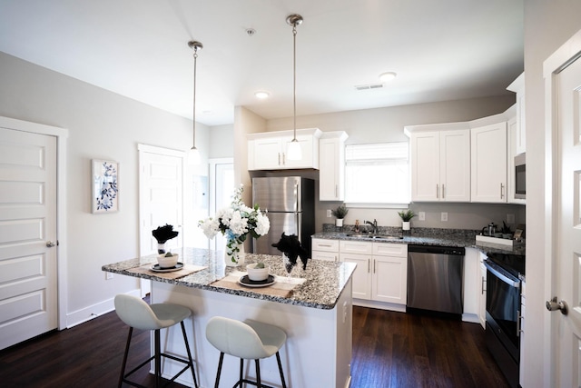 kitchen featuring sink, hanging light fixtures, stainless steel appliances, white cabinets, and a kitchen island