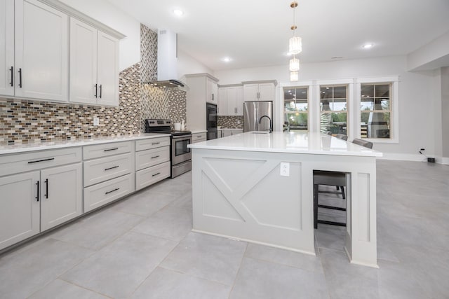 kitchen with hanging light fixtures, a center island with sink, appliances with stainless steel finishes, decorative backsplash, and wall chimney range hood