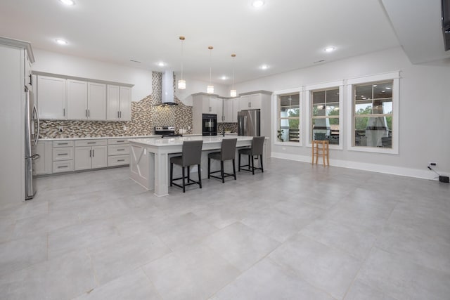 kitchen with appliances with stainless steel finishes, a breakfast bar, decorative light fixtures, a kitchen island with sink, and wall chimney range hood