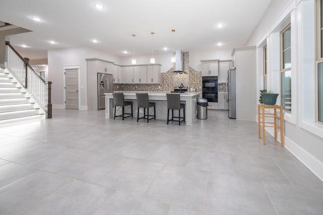 kitchen featuring a breakfast bar area, decorative light fixtures, stainless steel refrigerator, stainless steel fridge, and an island with sink