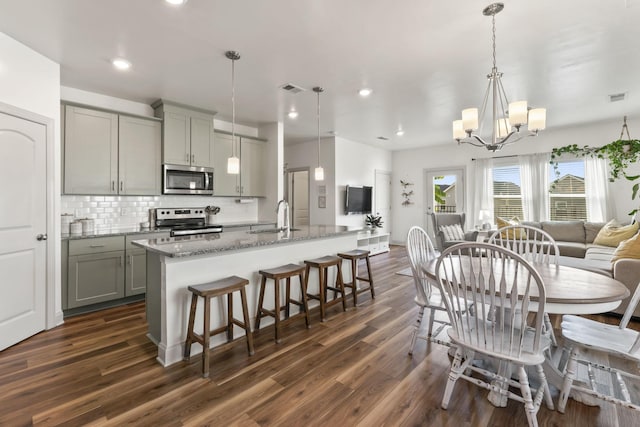 kitchen with sink, gray cabinetry, hanging light fixtures, light stone counters, and stainless steel appliances