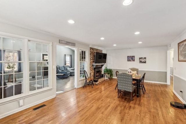 dining area featuring ornamental molding, a fireplace, and light hardwood / wood-style floors