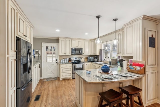 kitchen with decorative light fixtures, light wood-type flooring, appliances with stainless steel finishes, light stone countertops, and cream cabinetry