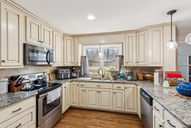 kitchen featuring cream cabinets, hardwood / wood-style floors, stainless steel appliances, and hanging light fixtures