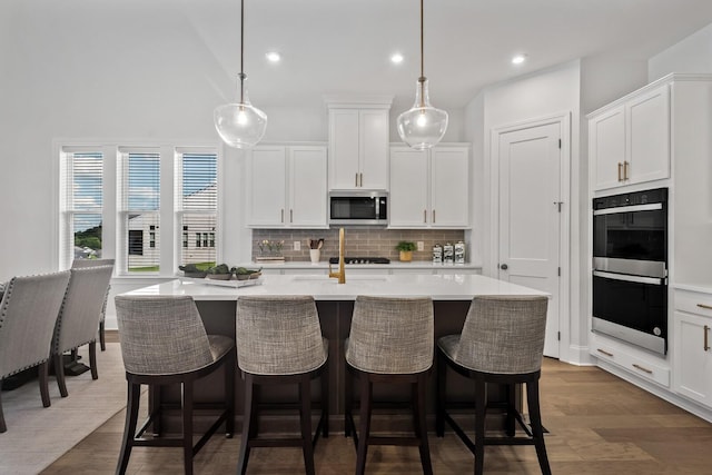 kitchen with pendant lighting, appliances with stainless steel finishes, an island with sink, and white cabinets