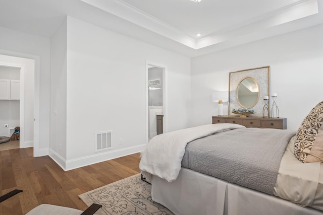 bedroom featuring ornamental molding, connected bathroom, hardwood / wood-style floors, and a tray ceiling