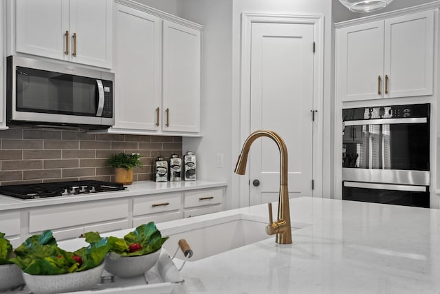 kitchen featuring appliances with stainless steel finishes, sink, white cabinets, decorative backsplash, and light stone countertops