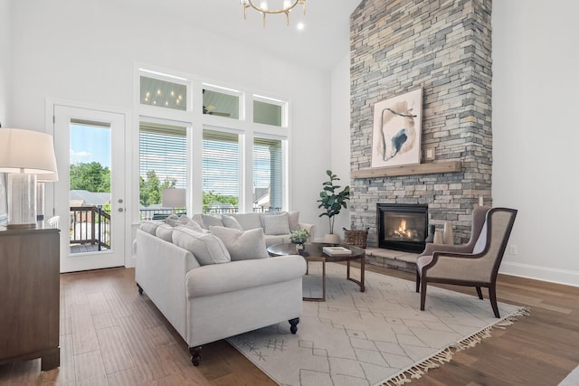 living room with wood-type flooring, a stone fireplace, plenty of natural light, and high vaulted ceiling