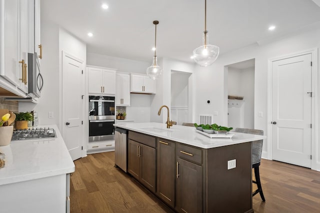 kitchen featuring a kitchen island with sink, sink, hanging light fixtures, and white cabinets