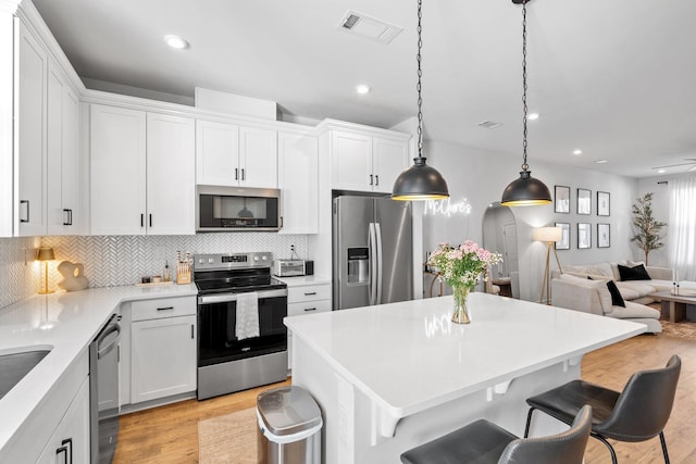 kitchen with stainless steel appliances, a kitchen breakfast bar, decorative backsplash, white cabinets, and decorative light fixtures