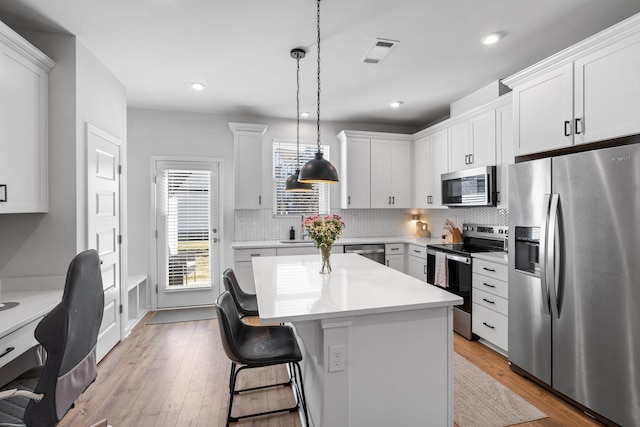 kitchen featuring white cabinetry, decorative light fixtures, appliances with stainless steel finishes, a kitchen island, and decorative backsplash