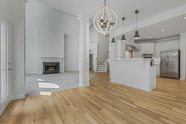 kitchen featuring white cabinetry, a kitchen island, pendant lighting, stainless steel appliances, and wall chimney range hood