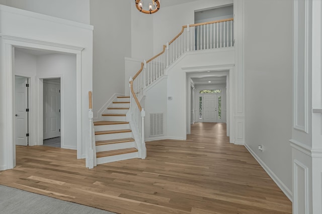 foyer featuring an inviting chandelier, a towering ceiling, and light wood-type flooring