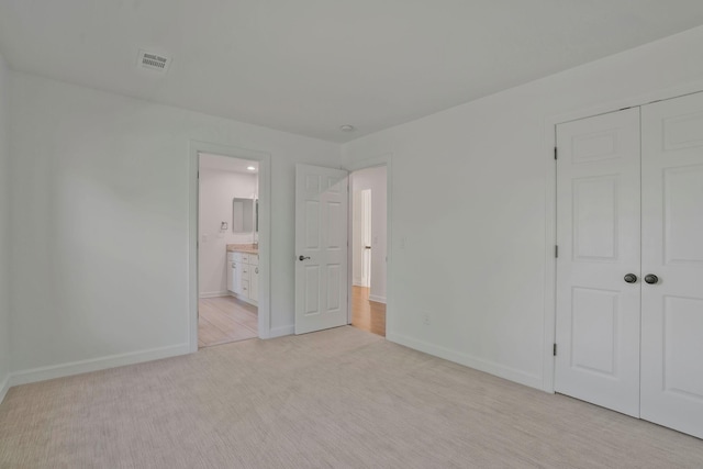 unfurnished bedroom featuring ensuite bathroom, light carpet, and a closet