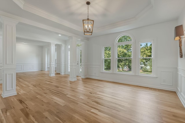 spare room with a tray ceiling, decorative columns, and light hardwood / wood-style floors