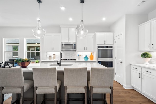 kitchen featuring tasteful backsplash, stainless steel appliances, an island with sink, and pendant lighting