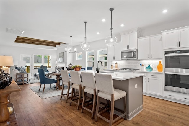 kitchen with stainless steel appliances, a center island with sink, white cabinets, and decorative light fixtures