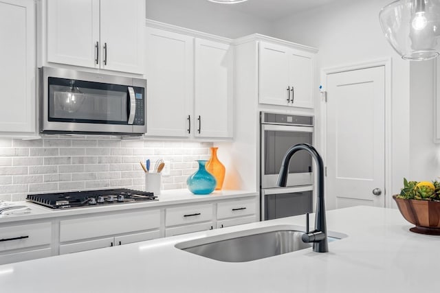 kitchen featuring sink, white cabinets, pendant lighting, stainless steel appliances, and backsplash