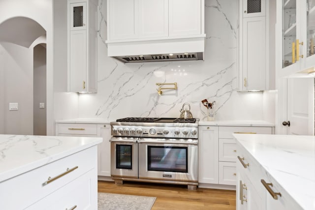 kitchen with white cabinetry, custom exhaust hood, double oven range, light stone countertops, and light hardwood / wood-style flooring